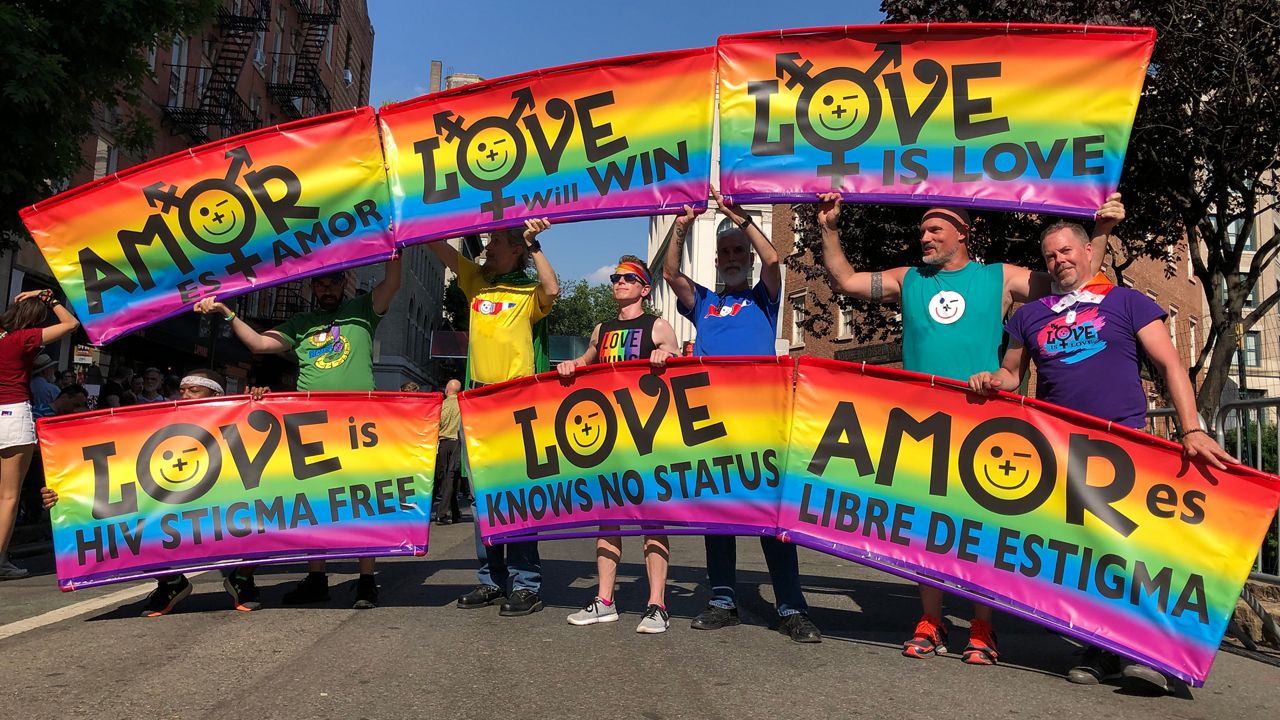 Six rainbow Pride flags held by people standing in a street.