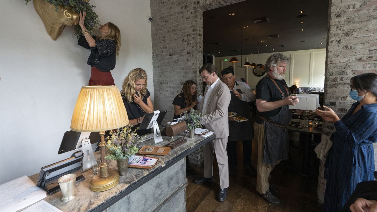 Caroline Styne, owner and wine director at The Lucques Group, top left, hangs a fresh floral wreath decoration to welcome customers, while her staff readies for arriving customers at the A.O.C. Brentwood restaurant in Los Angeles on June 19, 2021. (AP Photo/Damian Dovarganes)
