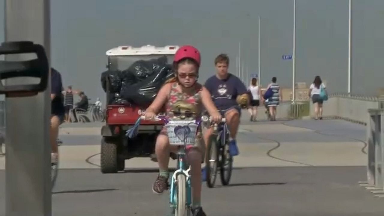 A girl wearing a pink bike helmet rides a bike in front of a boy on a bike.
