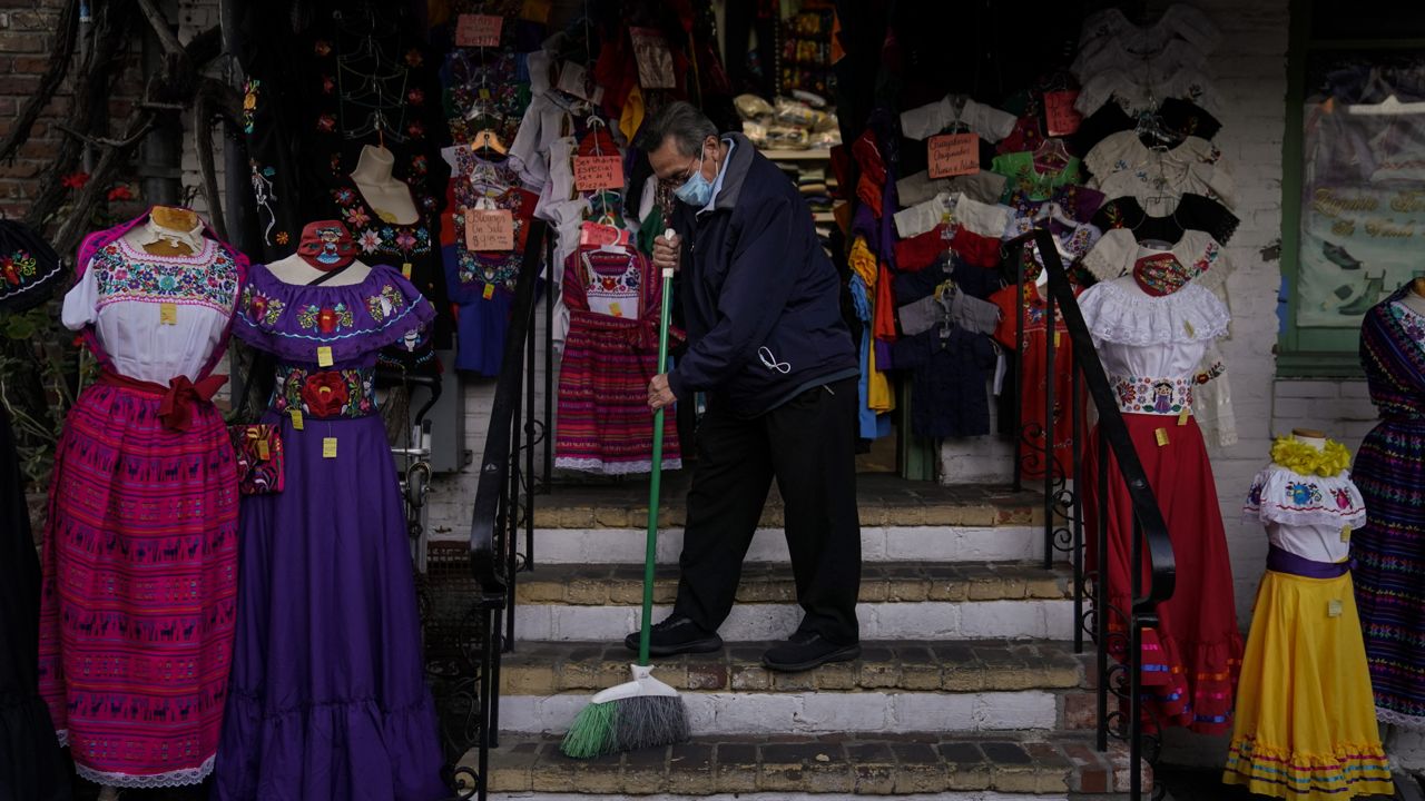 Victor Flores, 66, a third-generation owner of a gift shop, sweeps the steps of his store on Olvera Street in downtown Los Angeles, Wednesday, Dec. 16, 2020. (AP Photo/Jae C. Hong)