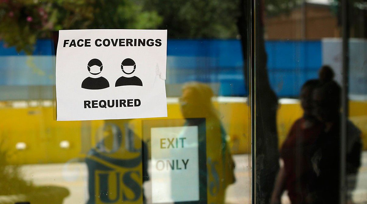 An image of a sign in a window that says "Face Coverings Required" (AP Image/File)