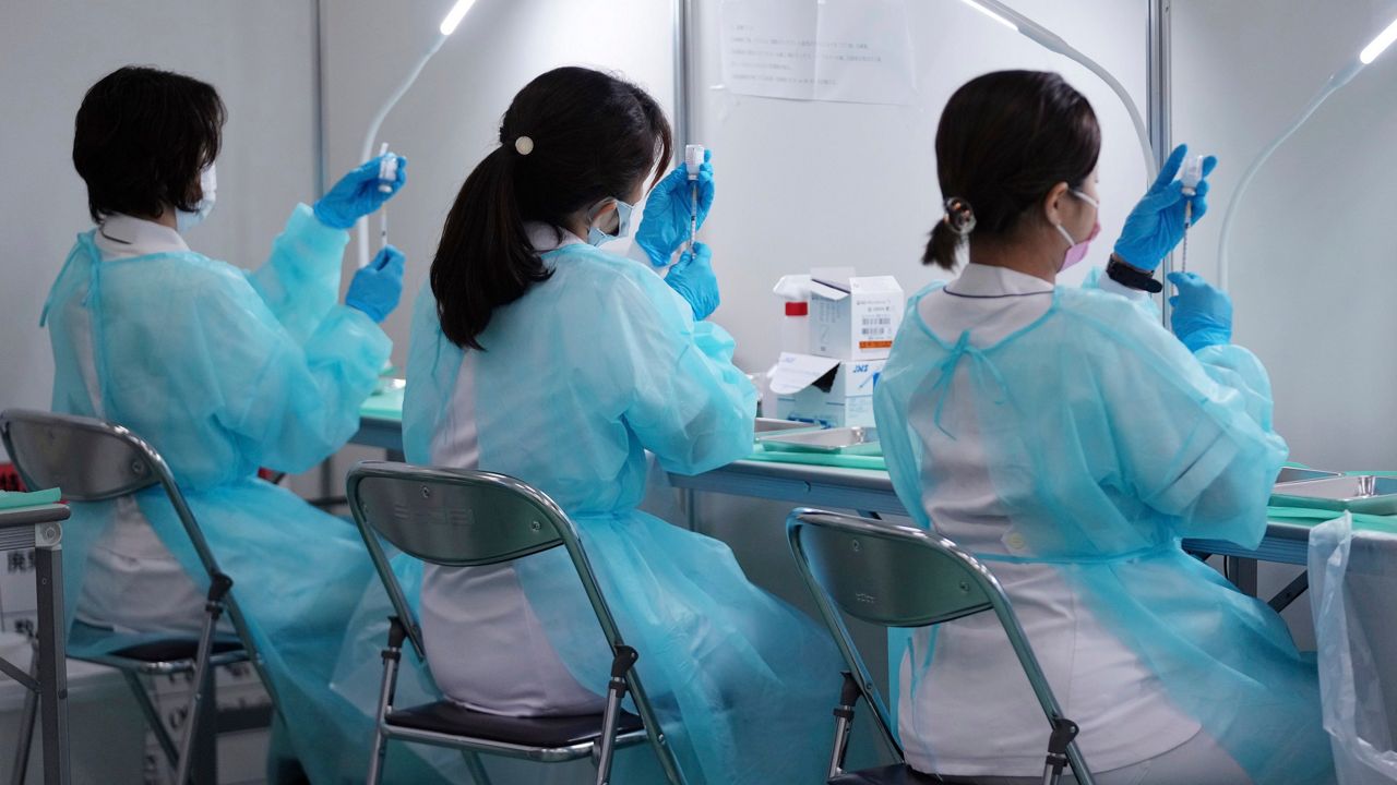 Three health care workers sit at a table, preparing vaccination syringes