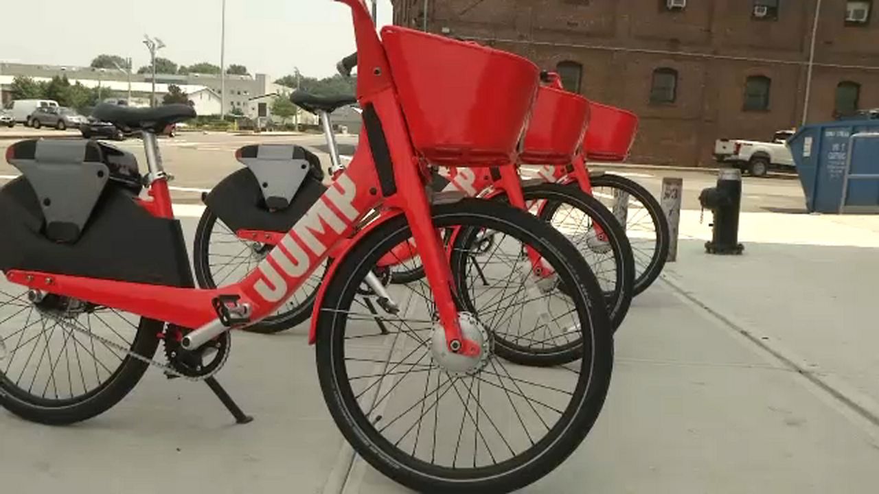 A line of red bikes with the "JUMP" logo in white text parked on a sidewalk.