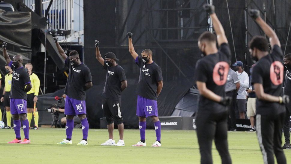 Orlando City players, left, raise their fists in the air in solidarity with other MLS teams before the start of an MLS soccer match, Wednesday, July 8, 2020, in Kissimmee, Fla., while wearing shirts and masks with messages about race. (AP Photo/John Raoux)