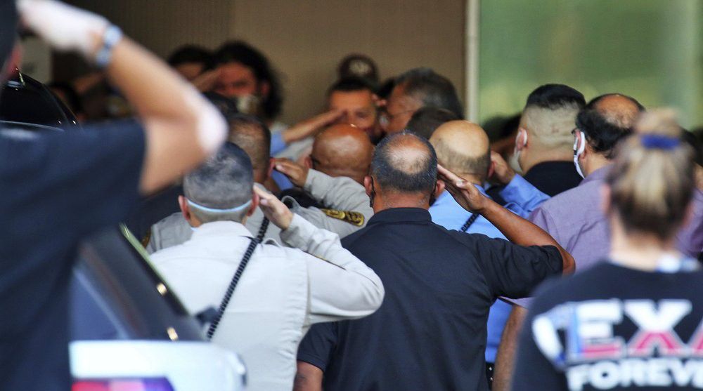 People salute as the body of a McAllen Police officer is carried out at McAllen Medical Center, Saturday, July 11, 2020, in McAllen, Texas. Two police officers were shot and killed after reportedly responding to a disturbance call. (Joel Martinez/The Monitor via AP)