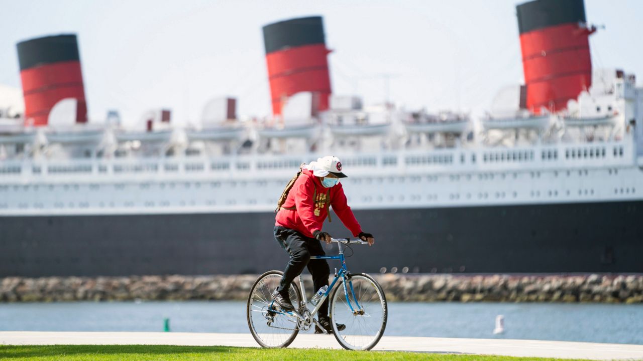 A bicyclist wearing a face mask rides past The Queen Mary hotel Monday, May 11, 2020, in Long Beach, Calif. (AP Photo/Ashley Landis)