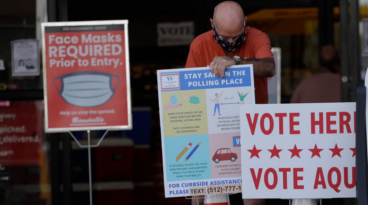 An election worker wearing a mask for protection against COVID-19 adjust signs for an early polling site located at a grocery store, Thursday, July 9, 2020, in Austin, Texas. (AP Photo/Eric Gay)