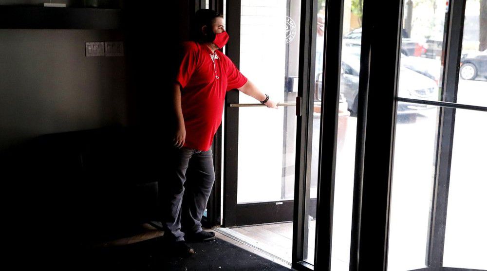 Wearing a mask amid concerns of the spread of the coronavirus, Dimitris Anagnostis opens the door to Chop House Burgers before the restaurant opened in downtown Dallas, Wednesday, July 8, 2020. (AP Photo/LM Otero)