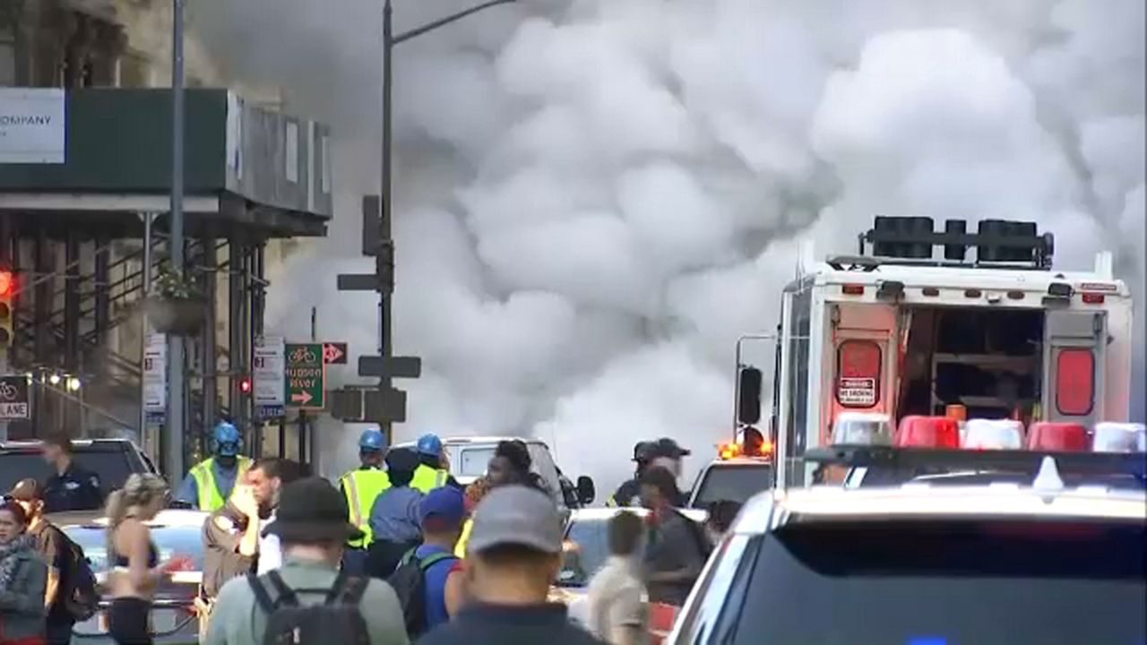 A cloud of steam near cars and a crowd of people.
