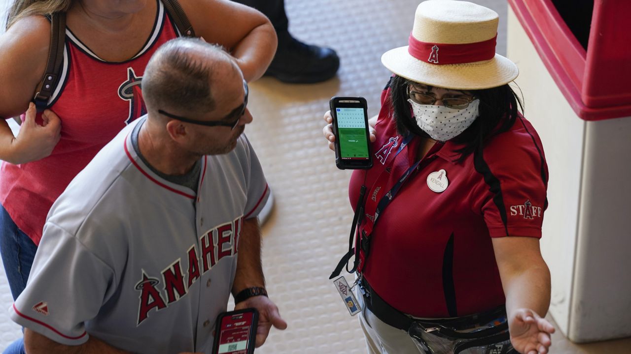 An employee of Angel Stadium directs fans through the front gate before a baseball game between the Boston Red Sox and the Los Angeles Angels Monday, July 5, 2021, in Anaheim, Calif. (AP Photo/Ashley Landis)