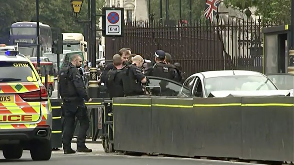 In this frame grab taken Tuesday, Aug. 14, 2018 armed police detain a man who was in a car that crashed into security barriers outside the Houses of Parliament stands to the right of a bus in London. London police say that a car has crashed into barriers outside the Houses of Parliament and that there are a number of injured. (ITN via AP)
