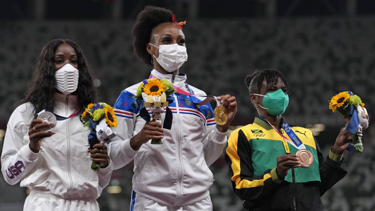 Gold medalist Jasmine Camacho-Quinn, centre, of Puerto Rico, stands with silver medalist Kendra Harrison, left, of the United States and bronze medalist Megan Tapper, of Jamaica after winning the women's 100-meters hurdles at the 2020 Summer Olympics, Monday, Aug. 2, 2021, in Tokyo. (AP Photo/Francisco Seco)
