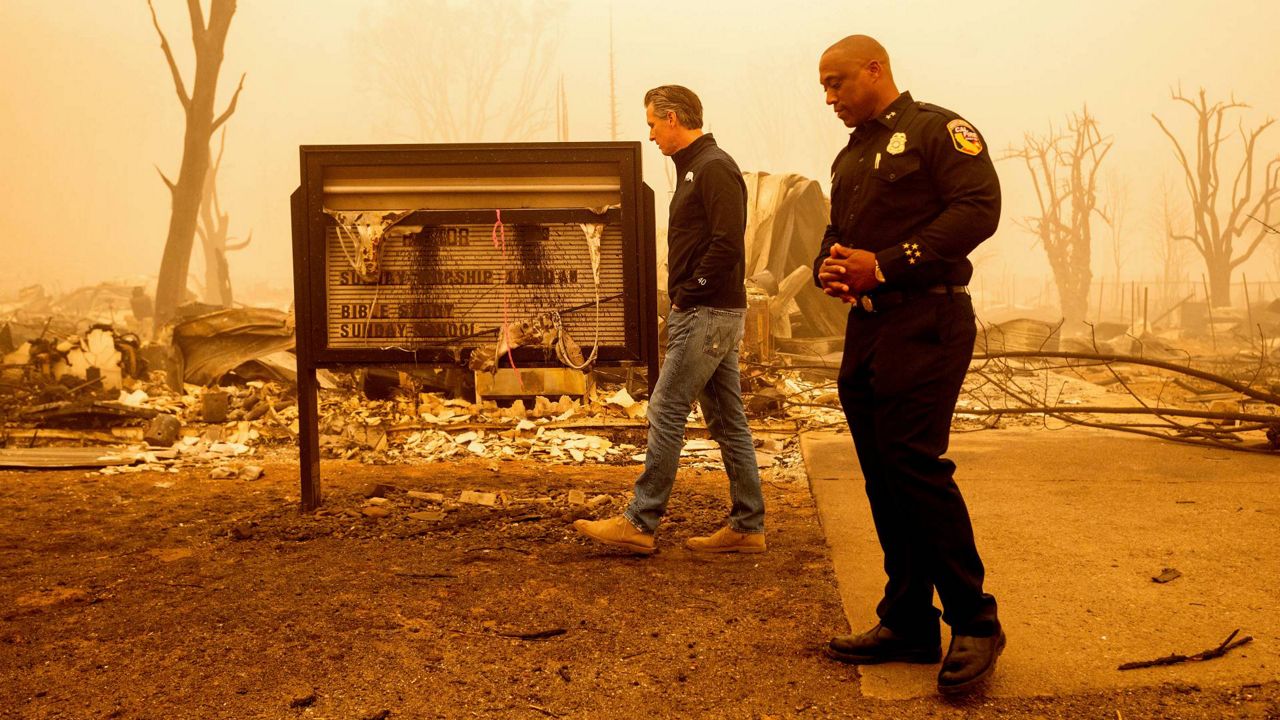 California Gov. Gavin Newsom examines a church marquee while visiting Greenville, which suffered extensive structure loss during the Dixie Fire, on Aug. 7, 2021, in Plumas County, Calif. (AP Photo/Noah Berger, File)