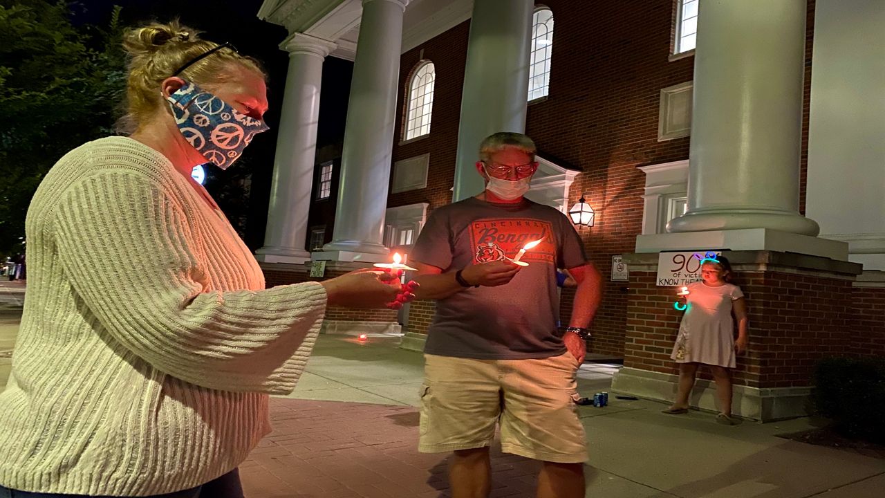 A man and woman hold candles at night in front of a courthouse