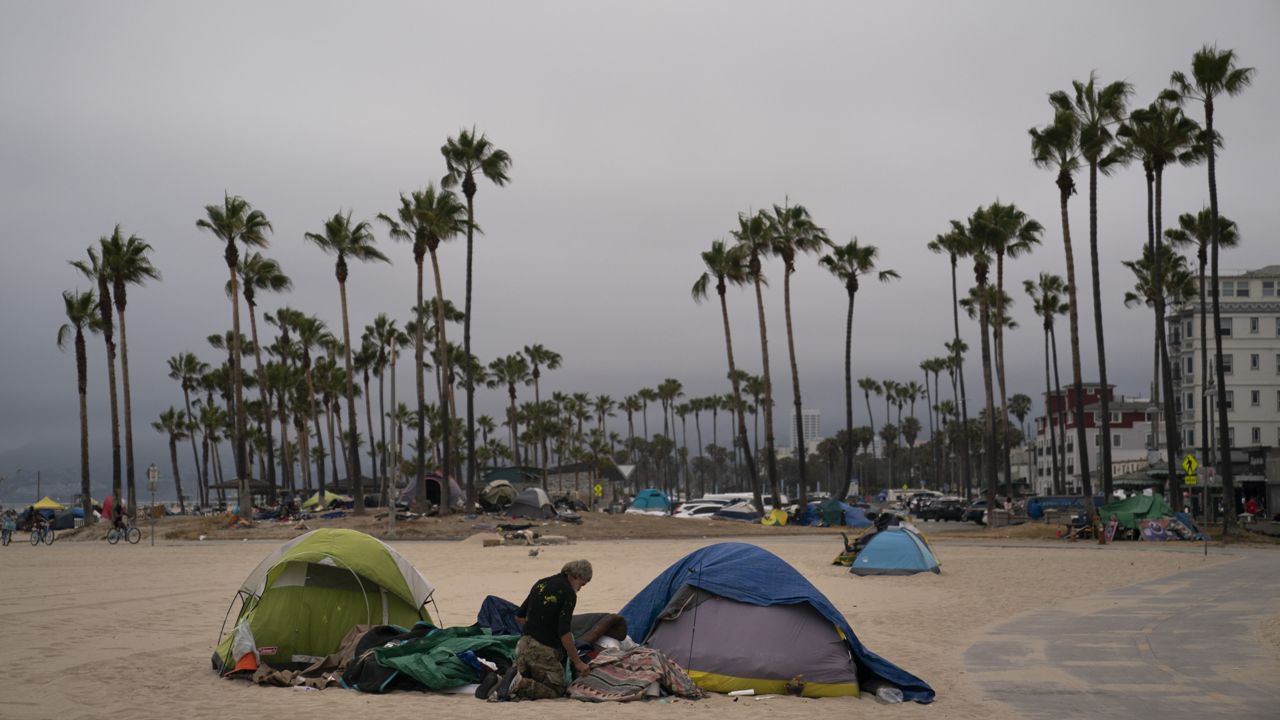 A homeless man goes through his belongings outside his tent pitched on the beach in the Venice neighborhood of Los Angeles, Tuesday, June 29, 2021. (AP Photo/Jae C. Hong)