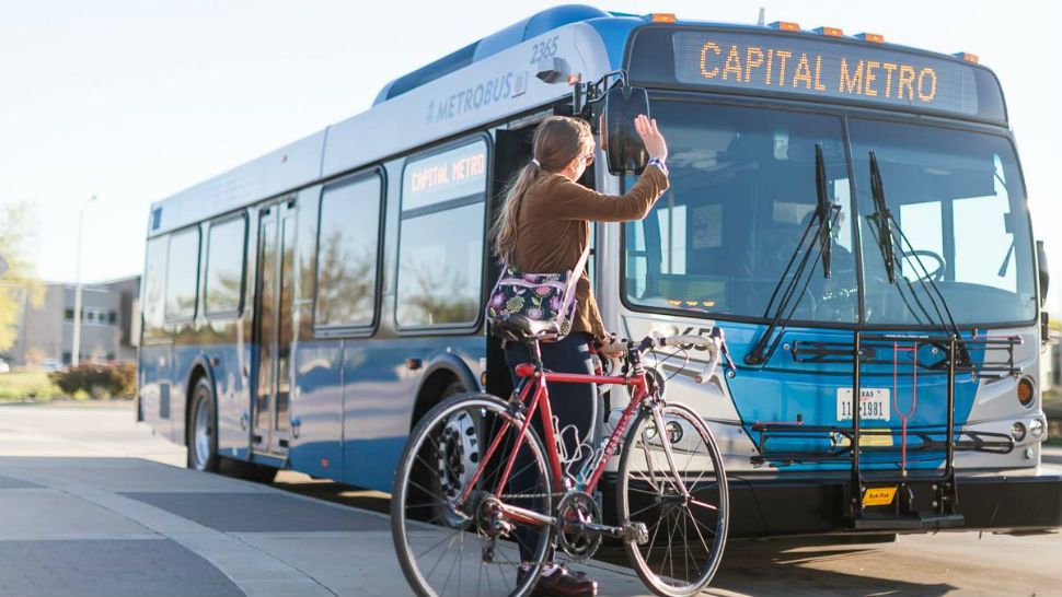 A woman on a red bicycle waves to a CapMetro bus. (Spectrum News file image)