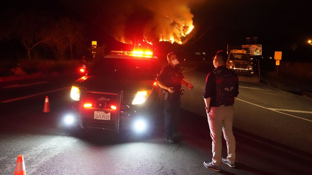 A highway patrolman talks to a resident at a road closure as the Ranch Fire burns, Thursday, Aug. 13, 2020, in Azusa, Calif. Heat wave conditions were making difficult work for fire crews battling brush fires and wildfires across Southern California. (Marcio Jose Sanchez/AP)