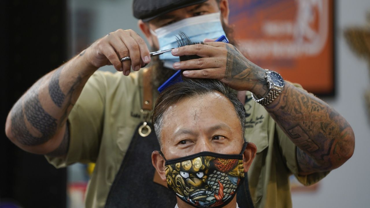 In this May 27, 2020 file photo Luis Lopez wears a face mask while giving a hair cut to Alexander Chin at Orange County Barbers Parlor in Huntington Beach, Calif. Orange County reported 342 new cases of COVID-19 and one additional death Sunday, bringing the county's totals to 43,709 cases and 810 deaths. (Ashley Landis/AP)