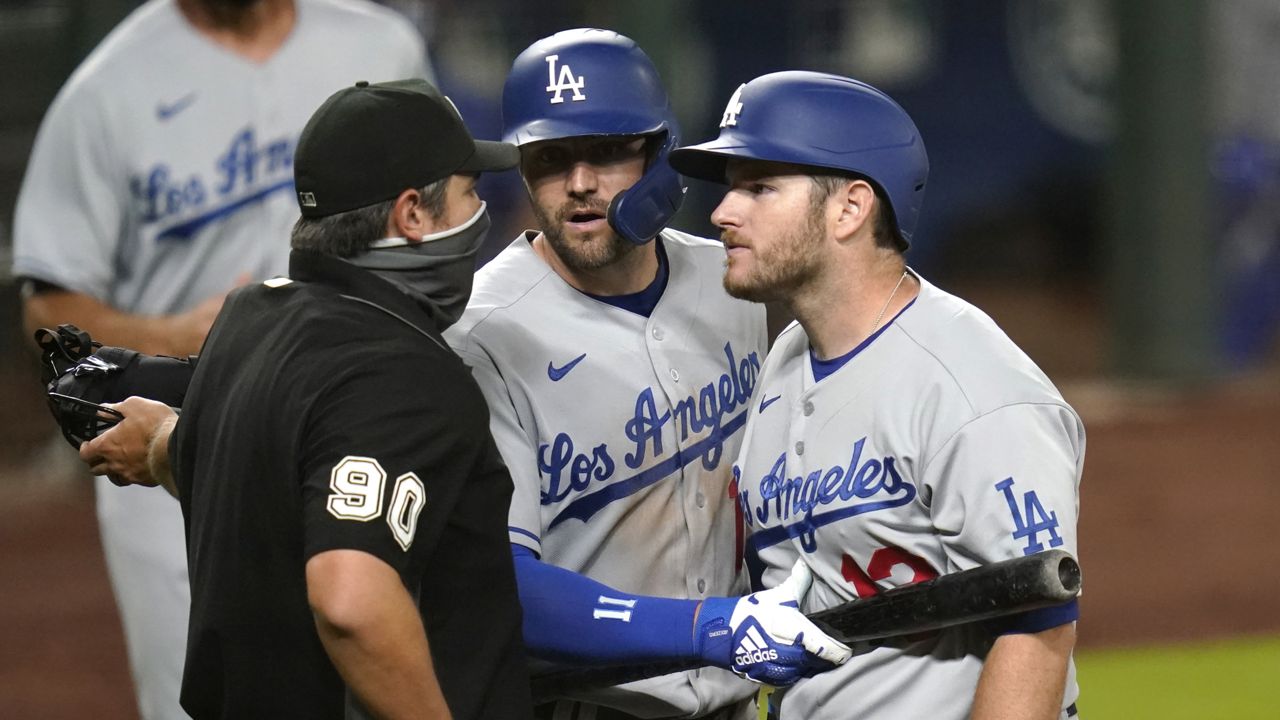 Los Angeles Dodgers' A.J. Pollock, center, uses his bat to nudge teammate Max Muncy, right, back as Muncy argues with home plate umpire Mark Ripperger after being ejected during the sixth inning of the team's baseball game against the Seattle Mariners on Wednesday, Aug. 19, 2020, in Seattle. (Elaine Thompson/AP)