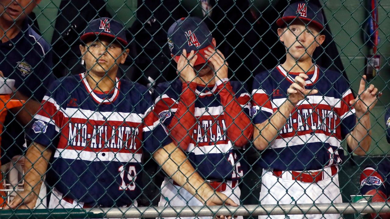 Three boys, wearing multi-colored jerseys, stand behind a wire fence.