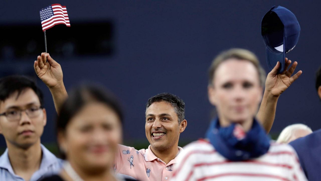 Ahmed Mahjoup, center, waves a flag after becoming a new U.S. citizen during a ceremony before a Dodgers game, Aug. 26, 2019, in San Diego. (AP Photo/Gregory Bull)