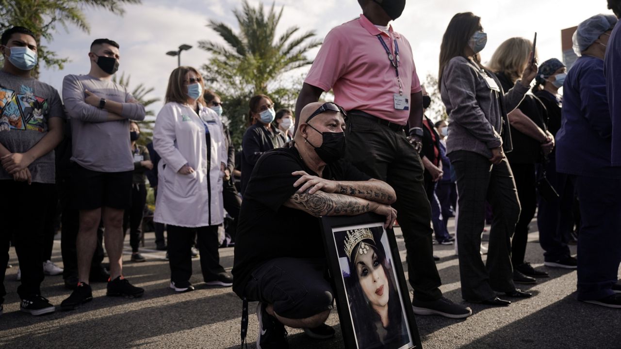 Rick Moran, kneeling, who lost his wife, Georgina, to COVID-19 last year, holds a framed photo of her as he is comforted by his colleague Wallace Pippen during an event held to honor health care workers and those who lost loved ones to the virus at Providence St. Jude Medical Center in Fullerton, Calif., Monday, May 10, 2021. (AP Photo/Jae C. Hong)