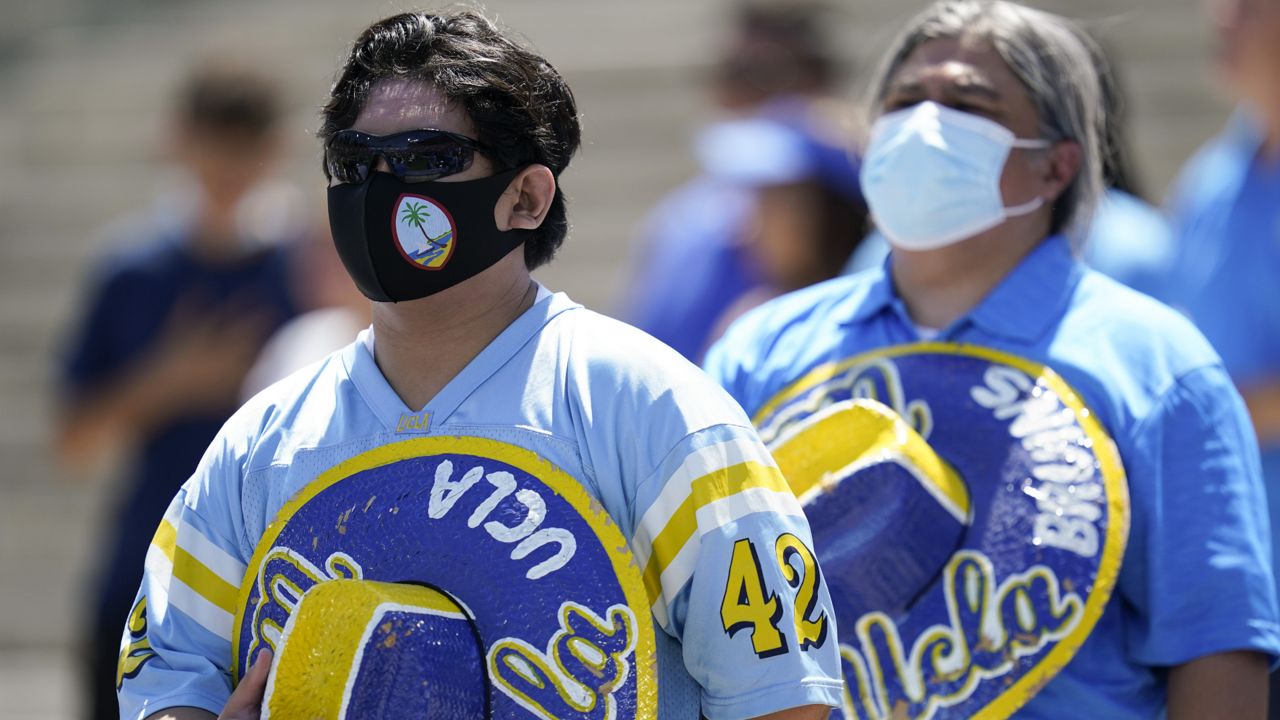 Fans wearing face masks stand as the national anthem plays before an NCAA college football game between Hawaii and UCLA, Saturday, Aug. 28, 2021, in Pasadena, Calif. (AP Photo/Ashley Landis)