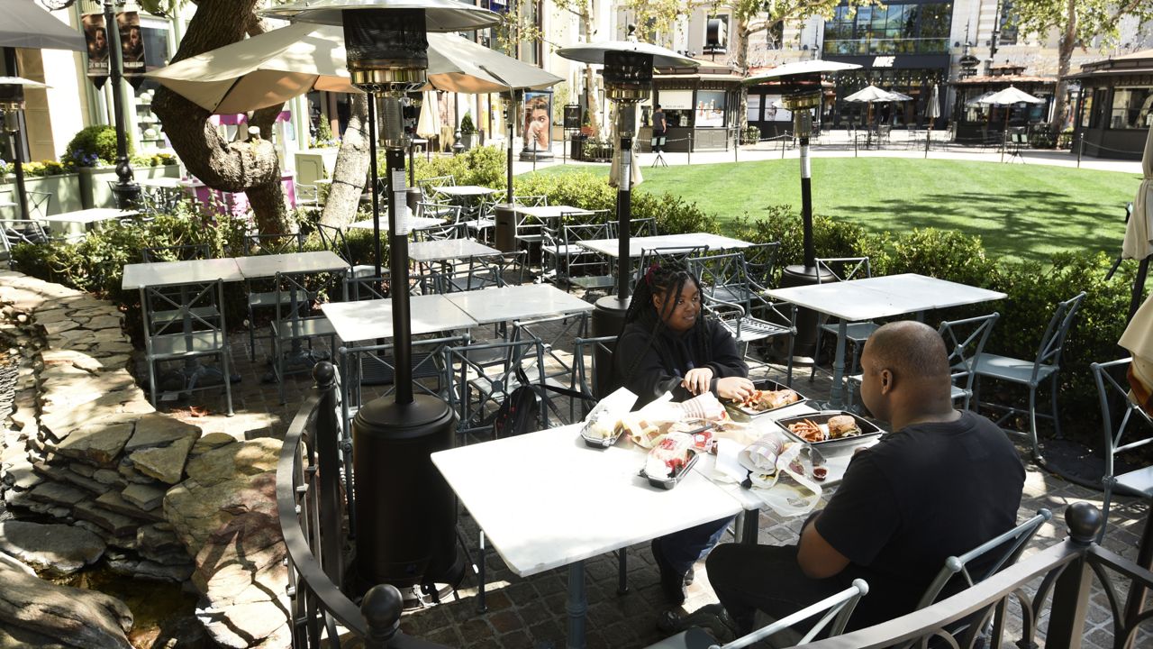 In this Aug. 18, 2020, file photo, Ashley Kelley, left, and Justin Sigler have lunch in a nearly empty outdoor dining area at the shopping and entertainment complex The Grove in Los Angeles. (AP Photo/Chris Pizzello,File)