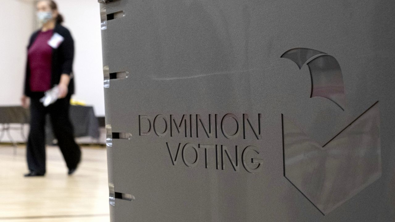 A worker passes a Dominion Voting ballot scanner while setting up a polling location at an elementary school in Gwinnett County, Ga., outside of Atlanta on Jan. 4, 2021. (AP Photo/Ben Gray)