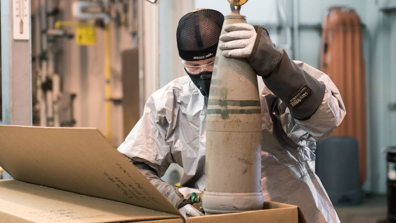 A munitions handler places a 155mm projectile containing mustard agent into a box to  begin the destruction process in the Static Detonation Chamber at the Blue Grass Chemical Agent-Destruction Pilot Plant. A portion of this photograph has been blurred in accordance with Department of Defense guidelines. (BGCAPP)