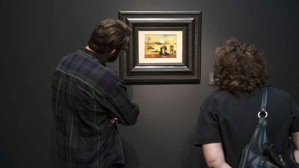 This Sept. 5, 2018 photo provided by the Meadows Museum at Southern Methodist University shows visitors looking at a Salvador Dali painting during an exhibit preview at the University's Meadows Museum in Dallas. The painting is part of an exhibit featuring the surrealist's lesser-known small scale paintings titled "Dali: Poetics of the Small," which opens Sunday. (Guy Rogers III/Meadows Museum/Southern Methodist University via AP)