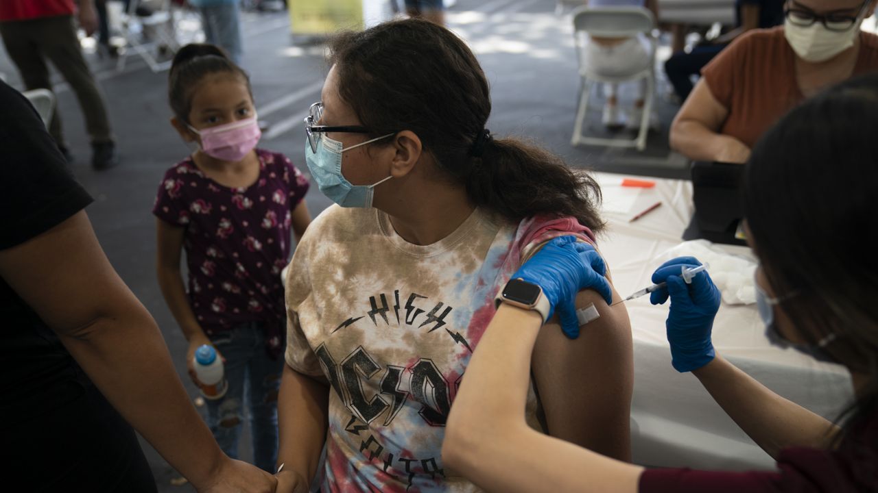 Holding her mother's hand, Brianna Vivar, 14, looks away while receiving the Pfizer COVID-19 vaccine from pharmacy technician Mary Tran at a vaccine clinic set up in the parking lot of CalOptima, Saturday, Aug. 28, 2021, in Orange, Calif. (AP Photo/Jae C. Hong)