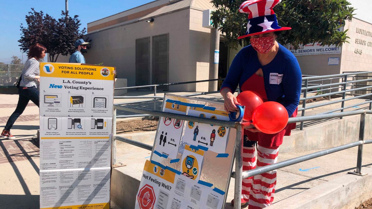 A volunteer at a polling place at the Montecito Heights Senior Citizen Center in Los Angeles adds balloons to voter information placards on Tuesday, Sept. 14, 2021. (AP Photo/Stefanie Dazio)