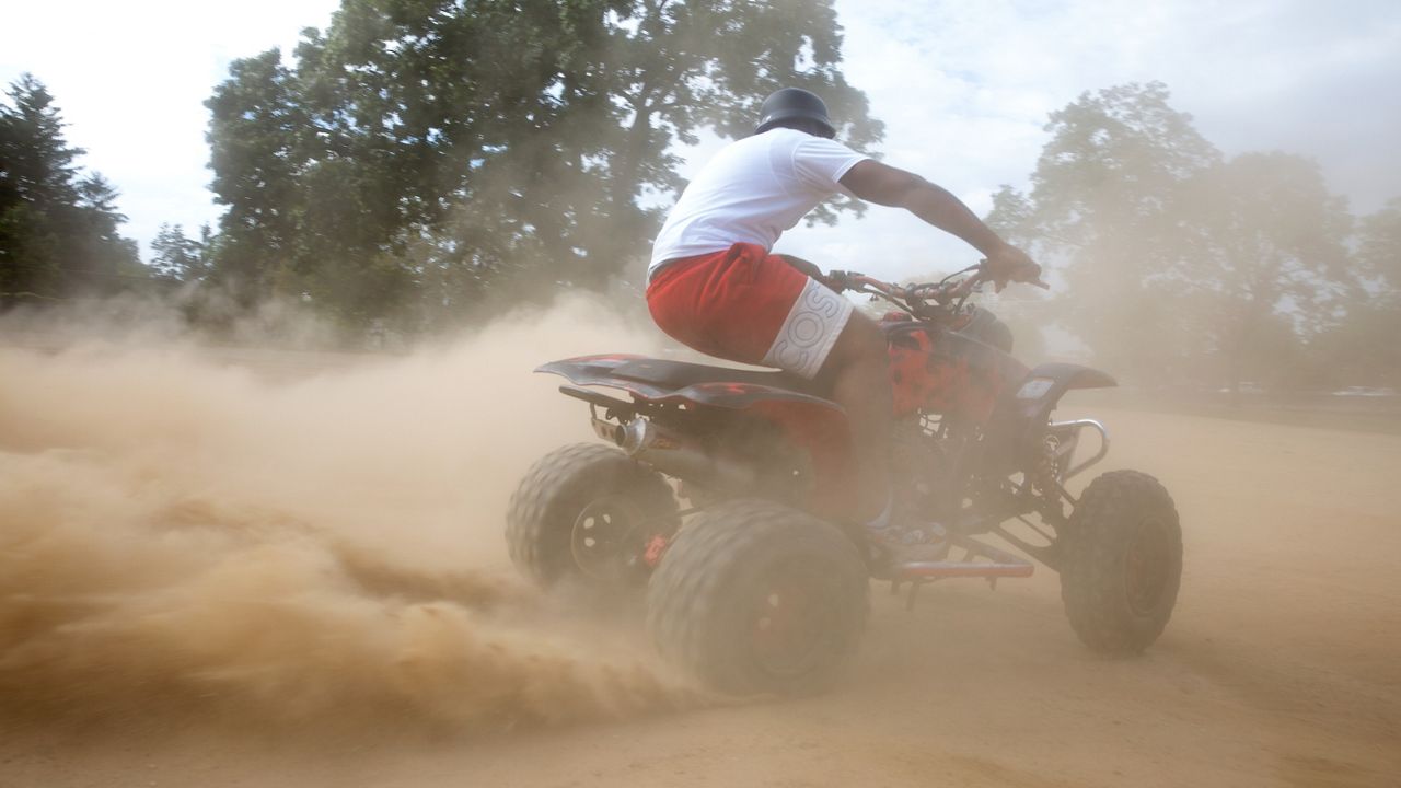 all terrain vehicle driver kicking up dust as he drives by the camera