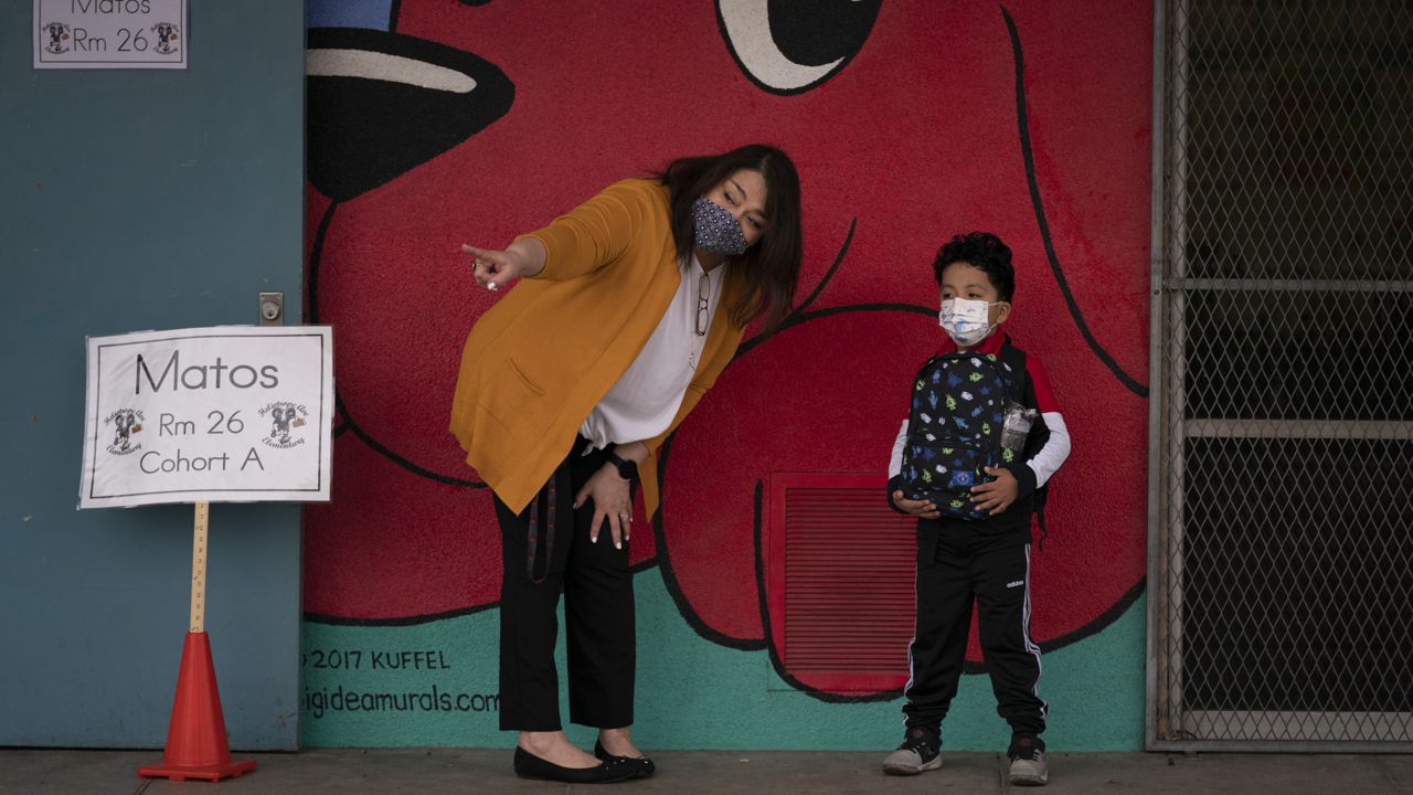 Kindergarten teacher Lilia Matos and her student Jesus Mendez stand outside their classroom on the first day of in-person learning at Heliotrope Avenue Elementary School in Maywood, Calif. on April 13, 2021. (AP Photo/Jae C. Hong)