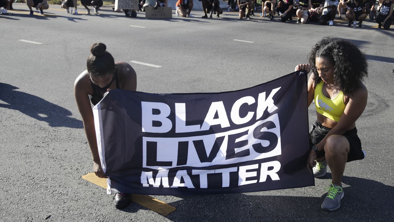 Alycia Pascual-Pena, left, and Marley Ralph kneel while holding a Black Lives Matter banner during a protest in memory of Breonna Taylor, Saturday, July 11, 2020, in Los Angeles.
