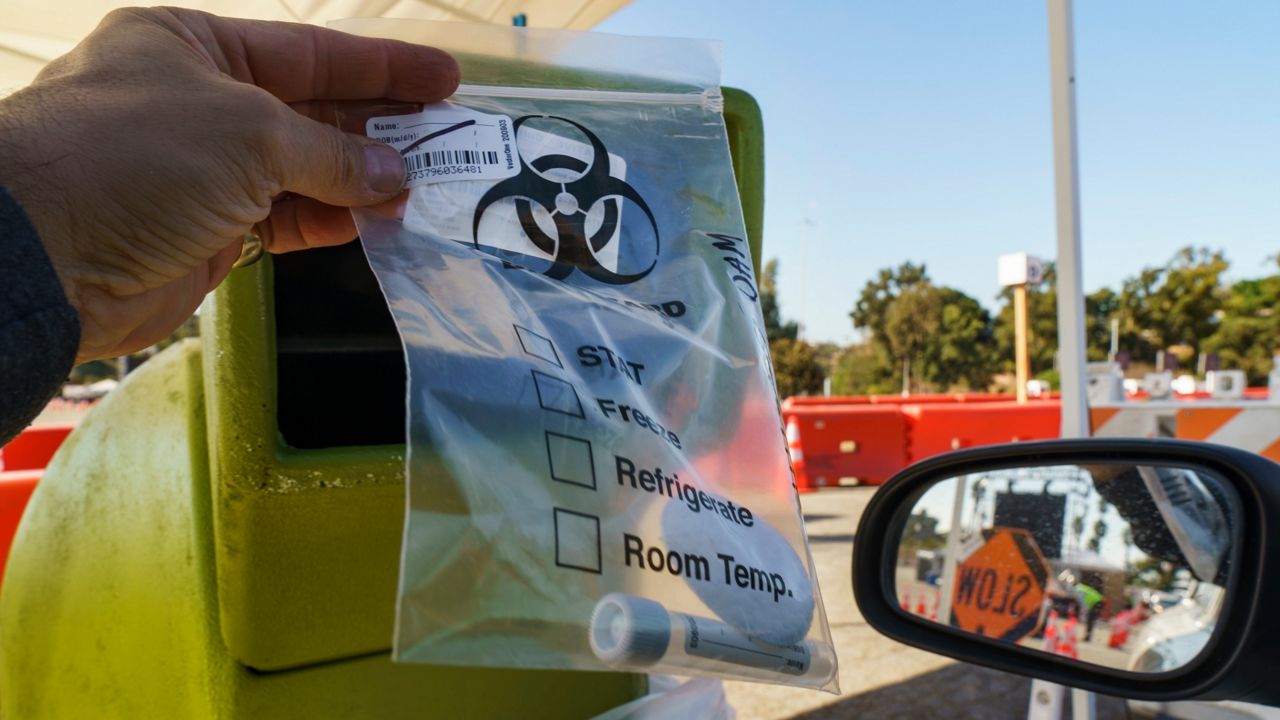 A completed COVID-19 virus self-test tube in a bag is dropped at a container at Dodger Stadium (AP Photo/Damian Dovarganes)