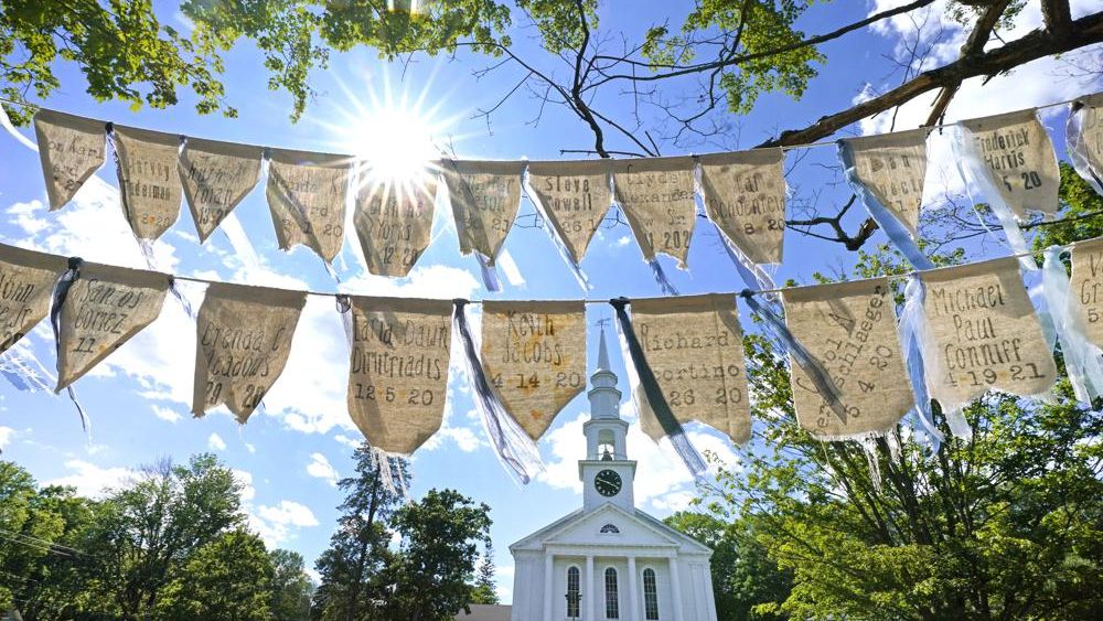 Flags with names of people who have died from COVID-19 are displayed outside the First Congressional Church, Thursday, June 17, 2021, in Holliston, Mass. The flags are part of the COVID Art and Remembrance project spearheaded by Jaclyn Winer, whose father, Keith Jacobs, died in April 2020 from the coronavirus. (AP Photo/Elise Amendola)