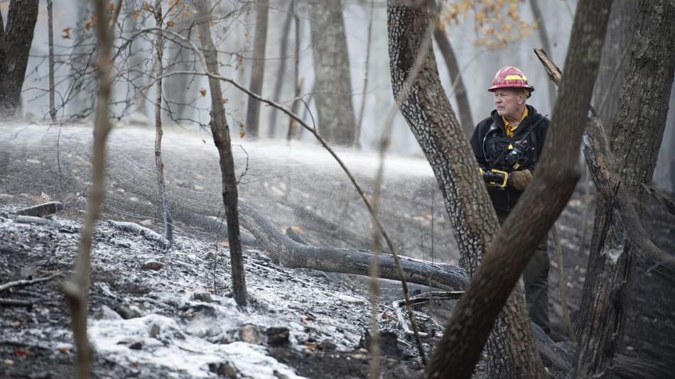 A firefighter with the North Carolina Forest Service sprays remaining hot spots from the wildfire at Pilot Mountain State Park that caused damage to over 1,000 acres by Tuesday, Nov. 30, 2021, in Pinnacle, N.C. (Allison Lee Isley/The Winston-Salem Journal via AP)