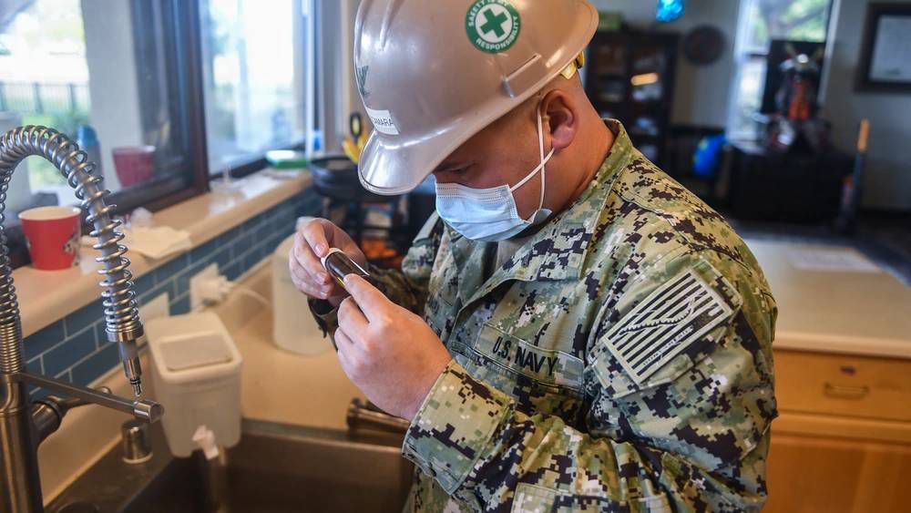 A military member inspects a water sample testing bottle during a field team home visit at a Joint Base Pearl Harbor-Hickam. (Credit: U.S. Navy)