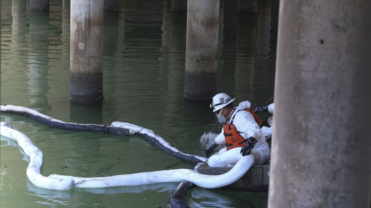 Workers in protective suits clean oil in an inlet leading to the Wetlands Talbert Marsh after an oil spill in Huntington Beach, Calif., on Tuesday, Oct. 5, 2021. (AP Photo/Ringo H.W. Chiu)