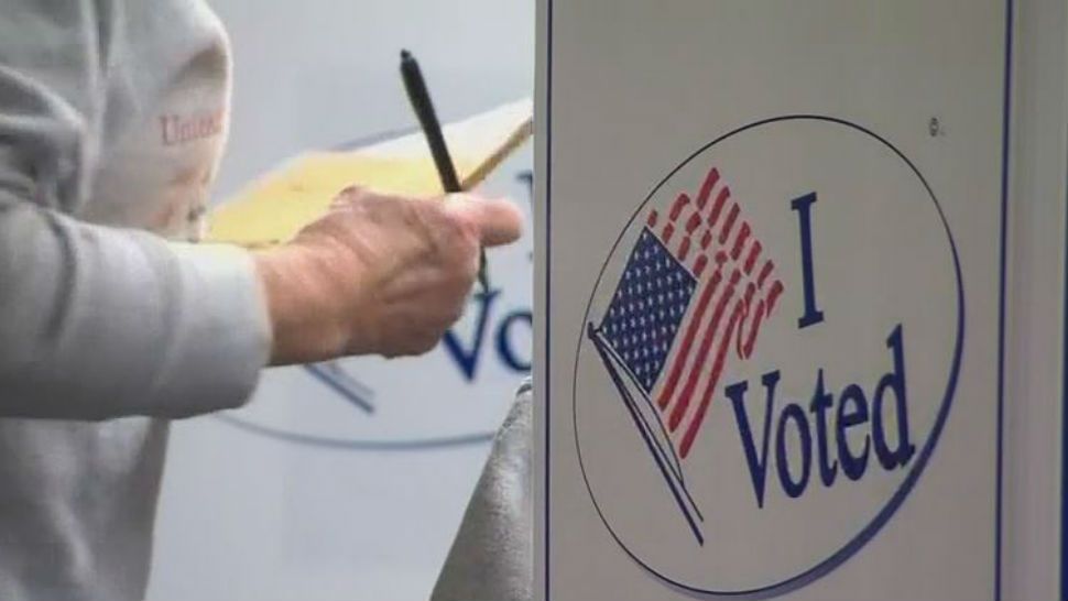 A woman stands at a voting booth with her ballot. 