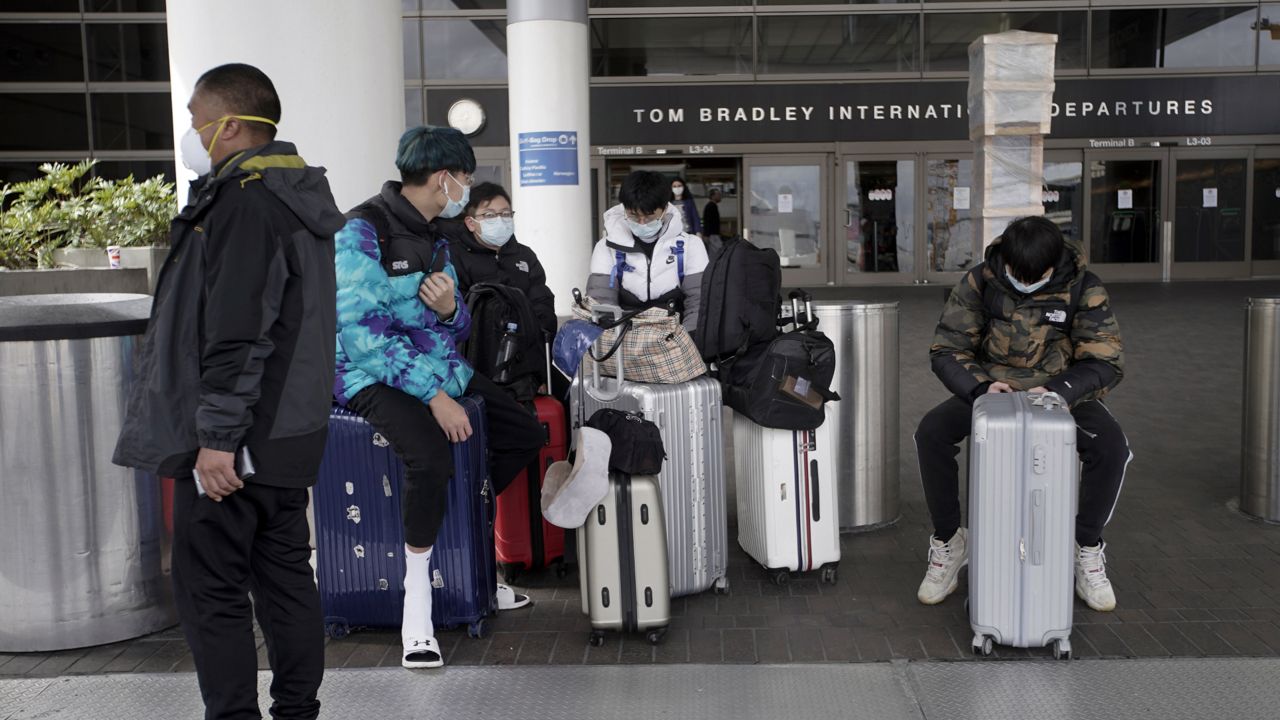 International travelers wait outside the Tom Bradley Terminal at the Los Angeles International Airport Tuesday, March 24, 2020, in Los Angeles. (AP Photo/Chris Carlson)