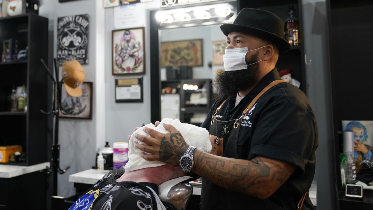 Luis Lopez, owner of Orange County Barbers Parlor, places a hot towel on Braunson McDonald on Wednesday, July 15, 2020, in Huntington Beach, Calif. (AP Photo/Ashley Landis)