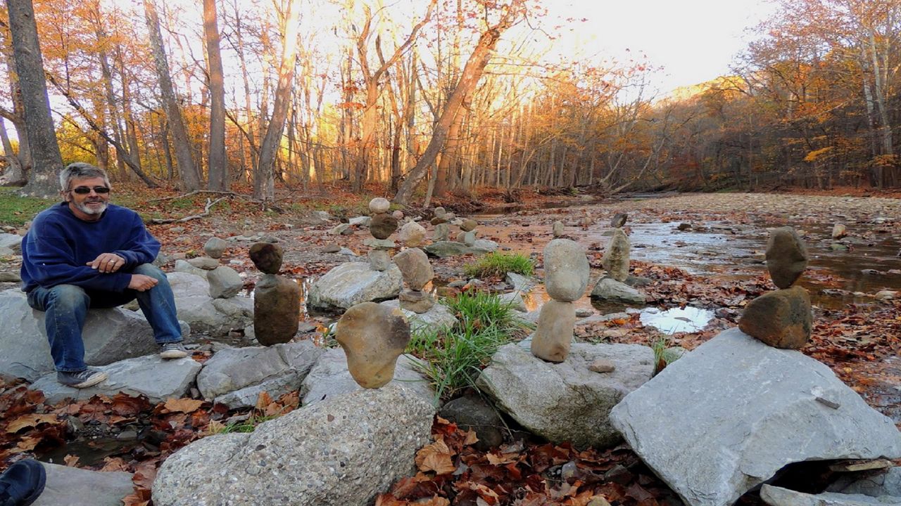 A man sits in the woods by stacked stones