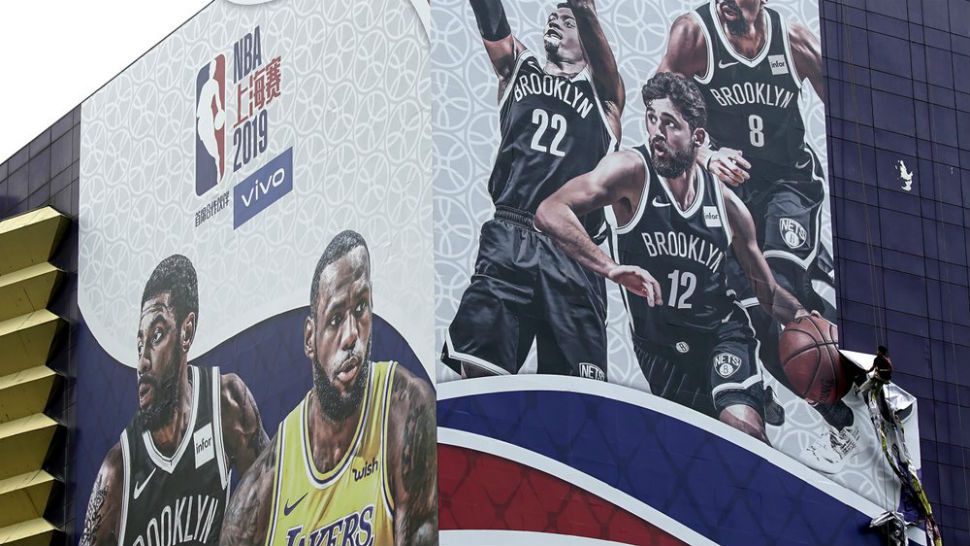 A worker takes down a billboard advertising an NBA preseason basketball game on Thursday between the Los Angeles Lakers and Brooklyn Nets in Shanghai, China, Wednesday, Oct. 9, 2019. The NBA has postponed Wednesday's scheduled media sessions in Shanghai for the Brooklyn Nets and Los Angeles Lakers, and it remains unclear if the teams will play in China this week as scheduled. (AP Photo)