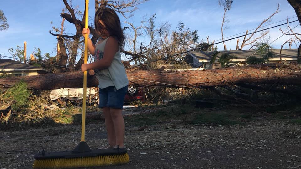 A young girl sweeps the street in front of her home in the Florida panhandle while her parents clean up debris from the carport. (Tony Rojek, Spectrum News)