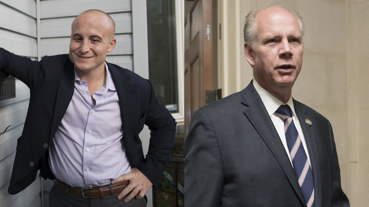 From left to right: A man, wearing a light purple dress shirt, dark pants, a brown belt, and a black blazer, leans his right arm against a black mailbox next to a white house; a man wearing a black suit jacket, a white dress shirt, and a navy blue-and-salmon-striped tie.