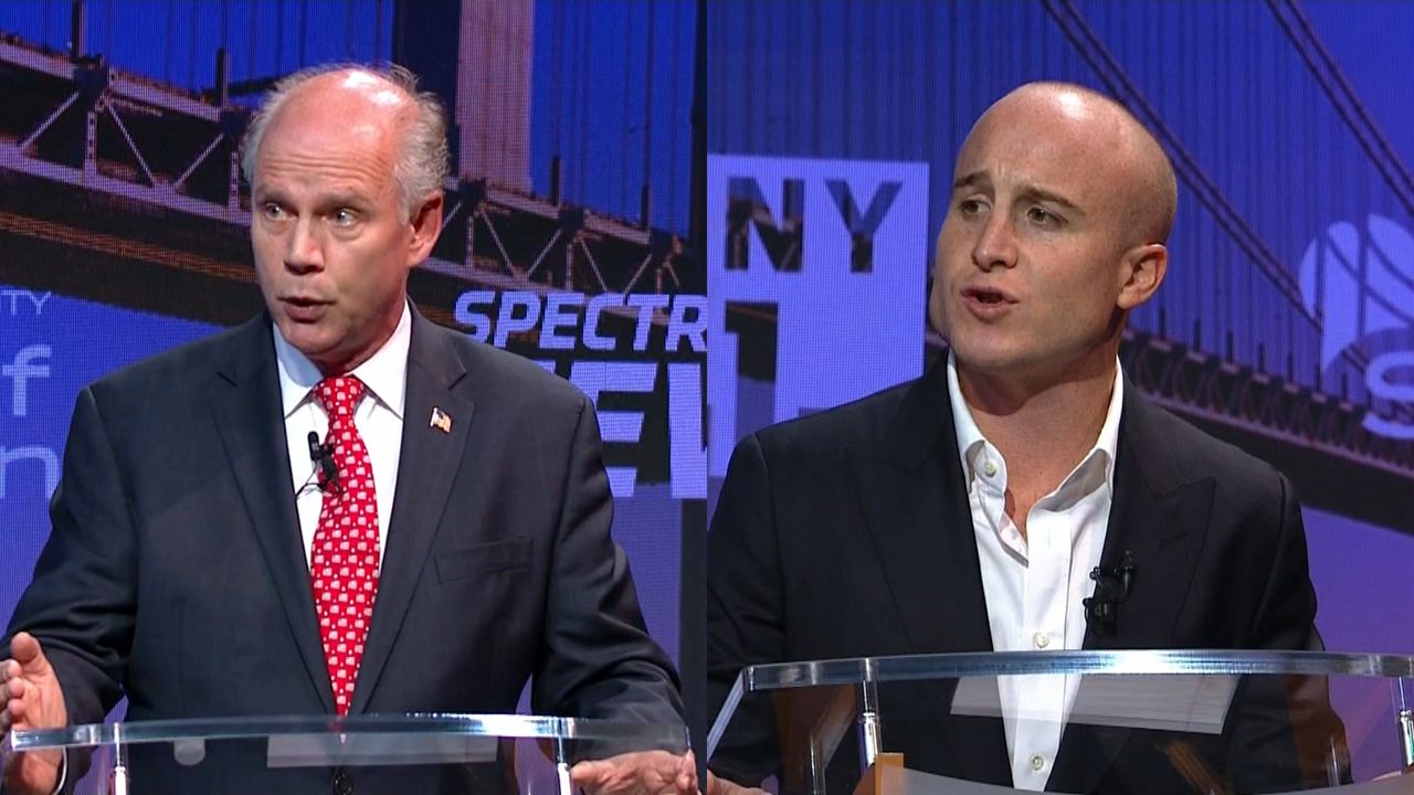 From left to right: A man wearing a black suit jacket, a white dress shirt, and a red tie with white spots; a man wearing a black blazer and a white dress shirt.