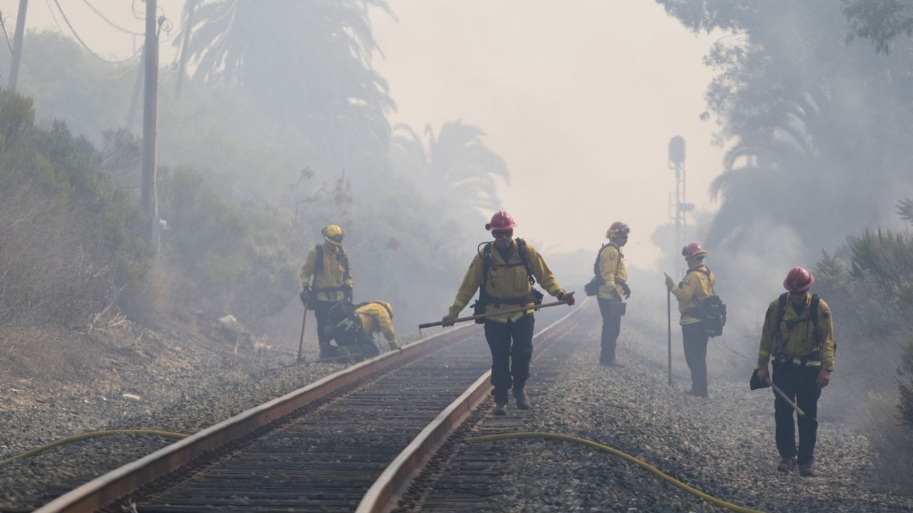 Firefighters look for roadside fires to extinguish next to train tracks off of the U.S. 101 highway Wednesday, Oct. 13, 2021, in Goleta, Calif. (AP Photo/Ringo H.W. Chiu)